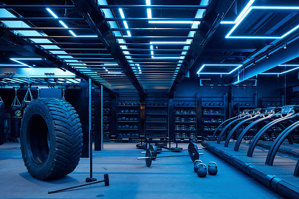 Cold blue light shining on exercise equipment in a fitness studio; tire, sledgehammer, treadmills, weights and more pictured