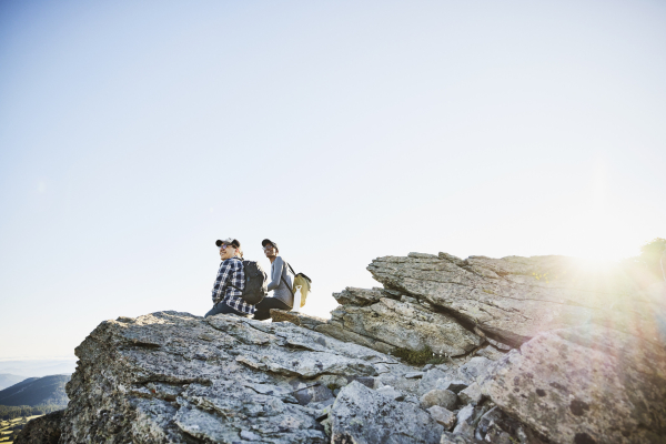 Two backpacking friends sitting on a craggy rock to enjoy the view during a sunrise hike 